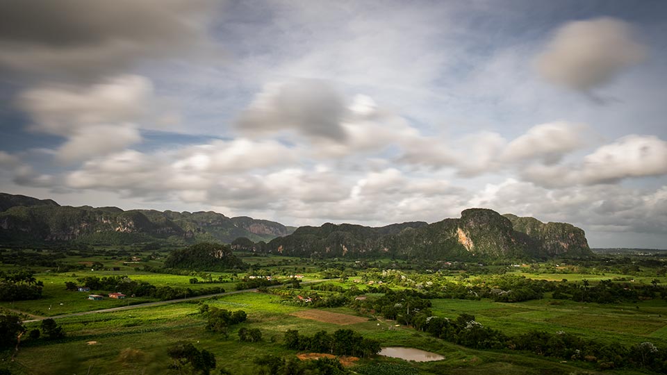 A view overlooking El Valle de Viñales or Viñales Valley. The village of Viñales can be seen on the right side of the photo on the horizon, hiding behind the trees.